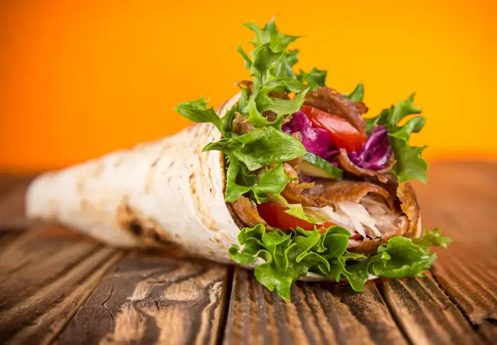 Kebab w tortilli z warzywami na drewnianym stole.