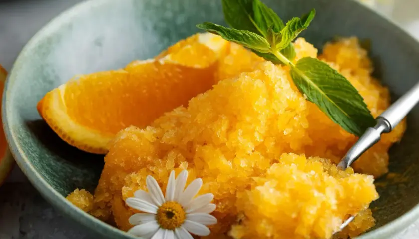 Pomarańczowy sorbet w misce z plasterkiem pomarańczy, miętą i kwiatkiem.